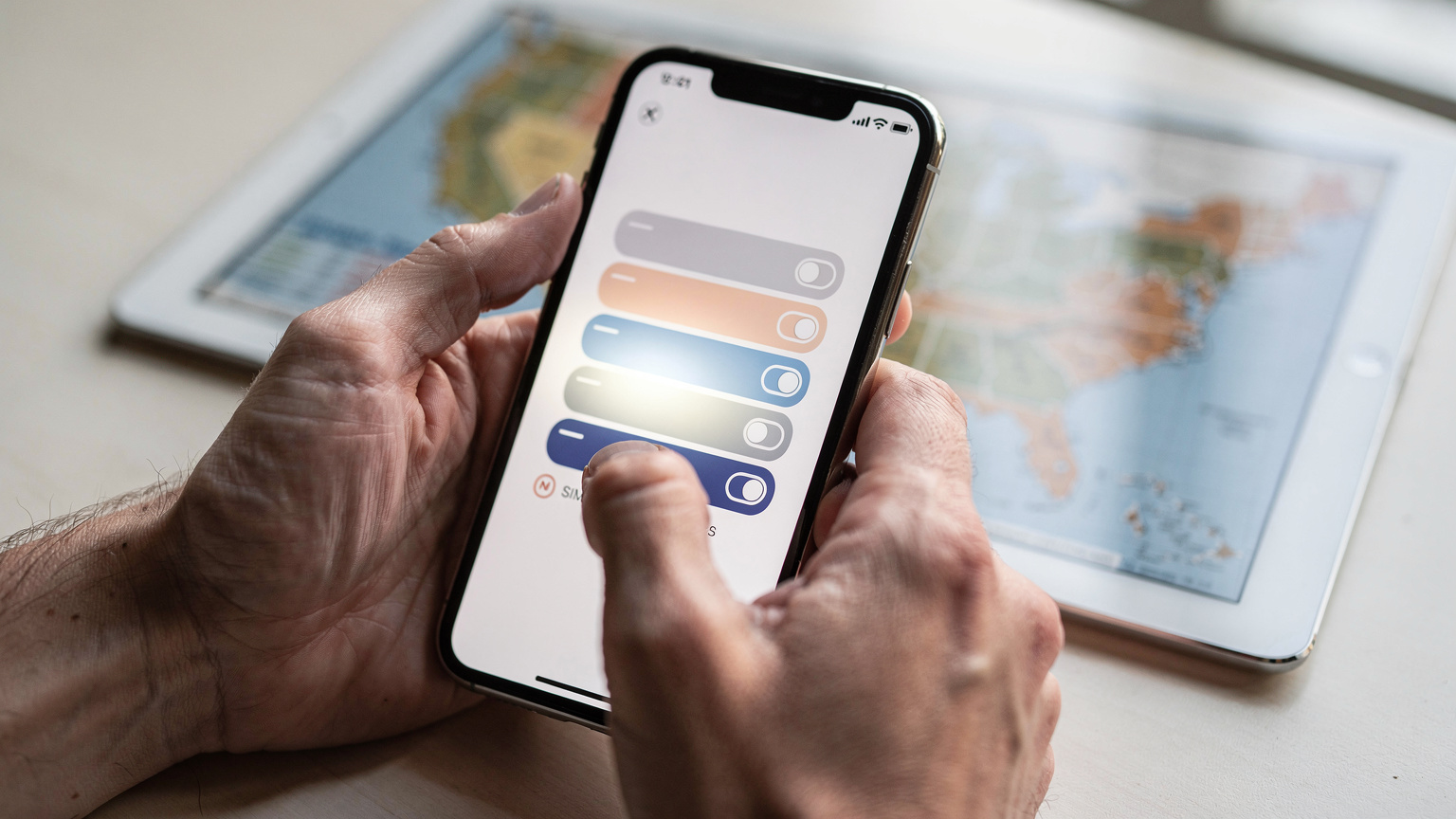 Manos de un viajero deslizando el dedo por la pantalla de un smartphone, mostrando la configuración de la eSIM con múltiples perfiles de red disponibles, con un mapa de Estados Unidos de fondo.
