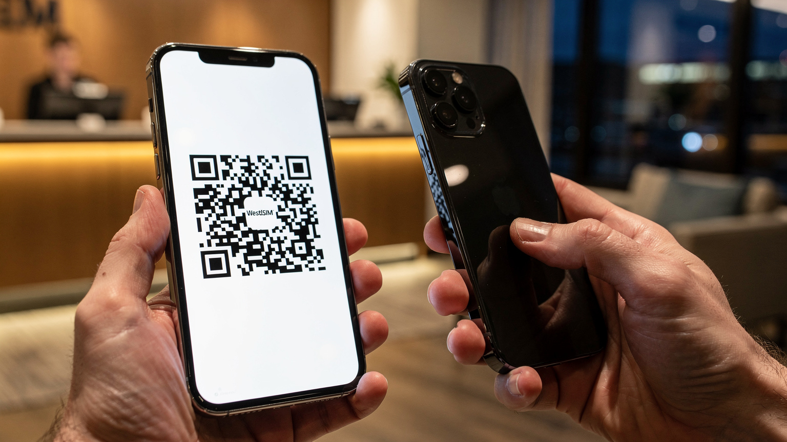 Close-up of human hands, one holding an iPhone 17 displaying a WestESIM QR code, the other holding a second smartphone scanning the code. The setting is a cozy, well-lit corner of a hotel lobby in downtown Vancouver, British Columbia, with a subtle backdrop of a modern check-in desk.