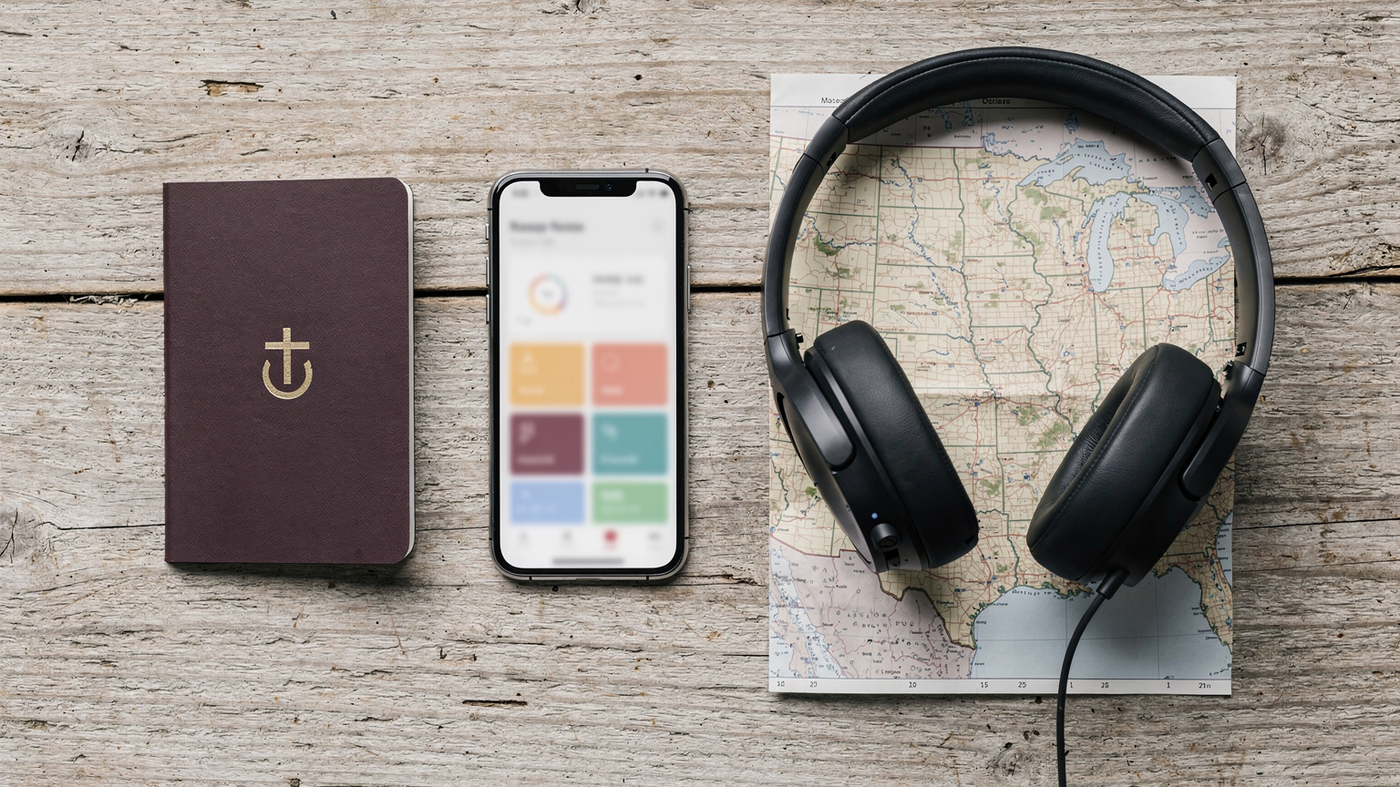 An editorial flat-lay shot on a rustic wooden table featuring a passport, a smartphone displaying a travel app, noise-canceling headphones, and a US physical map snippet, all bathed in soft, natural light.