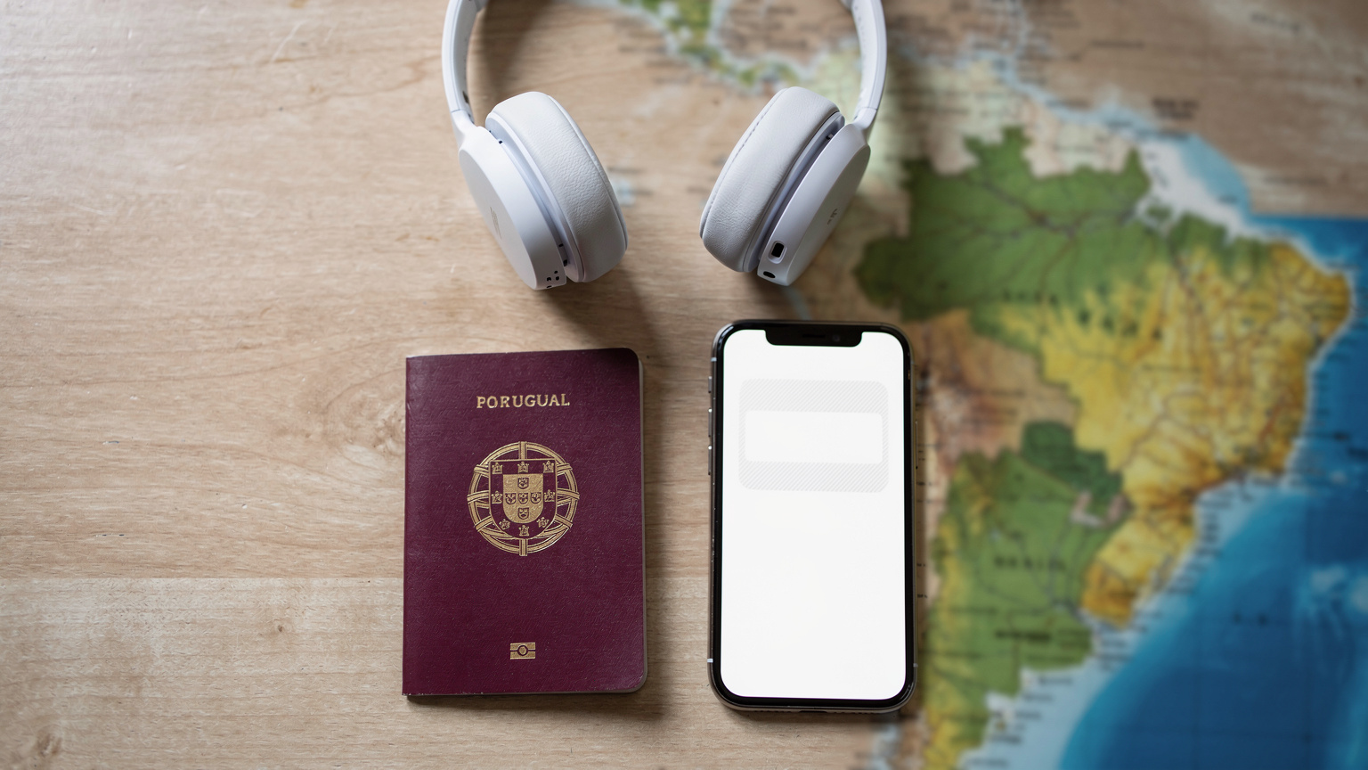 Uma mesa de café com um passaporte português, um smartphone com um eSIM e alguns fones de ouvido, com um mapa do Brasil em segundo plano, em um estilo de flat-lay editorial.