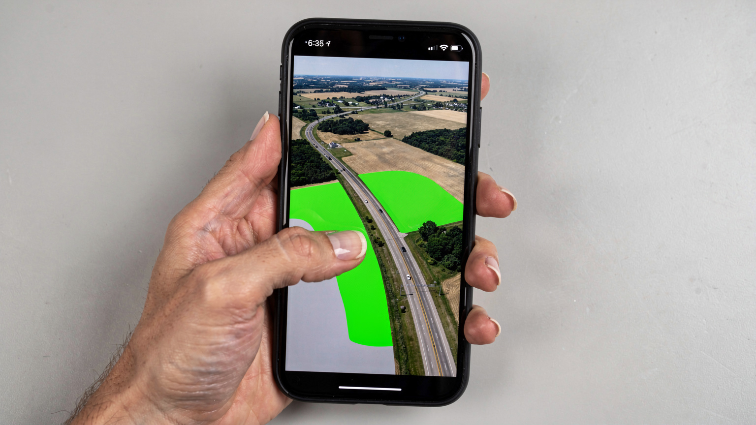 A person's hand with a manicured nail is using a smartphone to zoom into a T-Mobile coverage map, specifically highlighting a rural highway section in the Midwest with potential gaps in service.